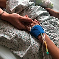 caring adult holding hand of child with IV
